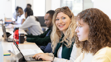 une étudiante assise devant son ordinateur sourit